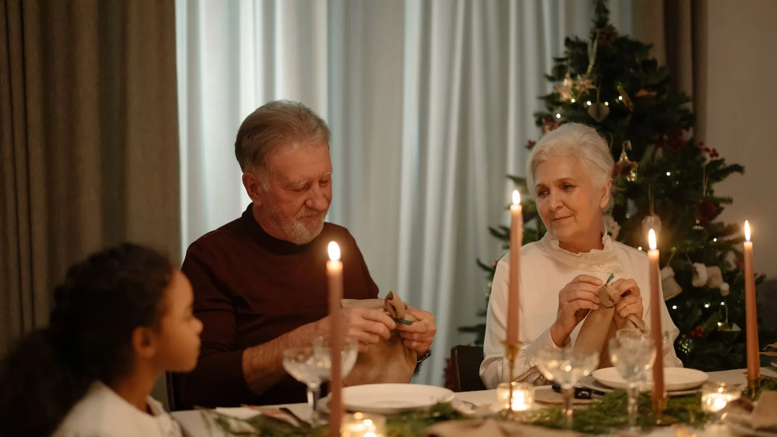 Casal de idosos e neta reunidos à mesa decorada em celebração de Natal em família