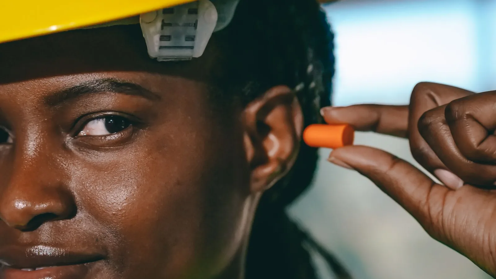 Trabalhador com capacete de segurança colocando protetor auricular