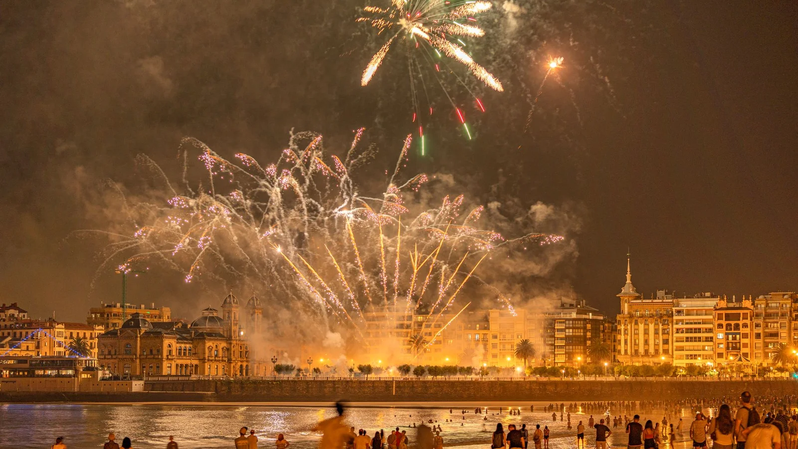 Pessoas na praia à noite assistindo a uma queima de fogos de artifício