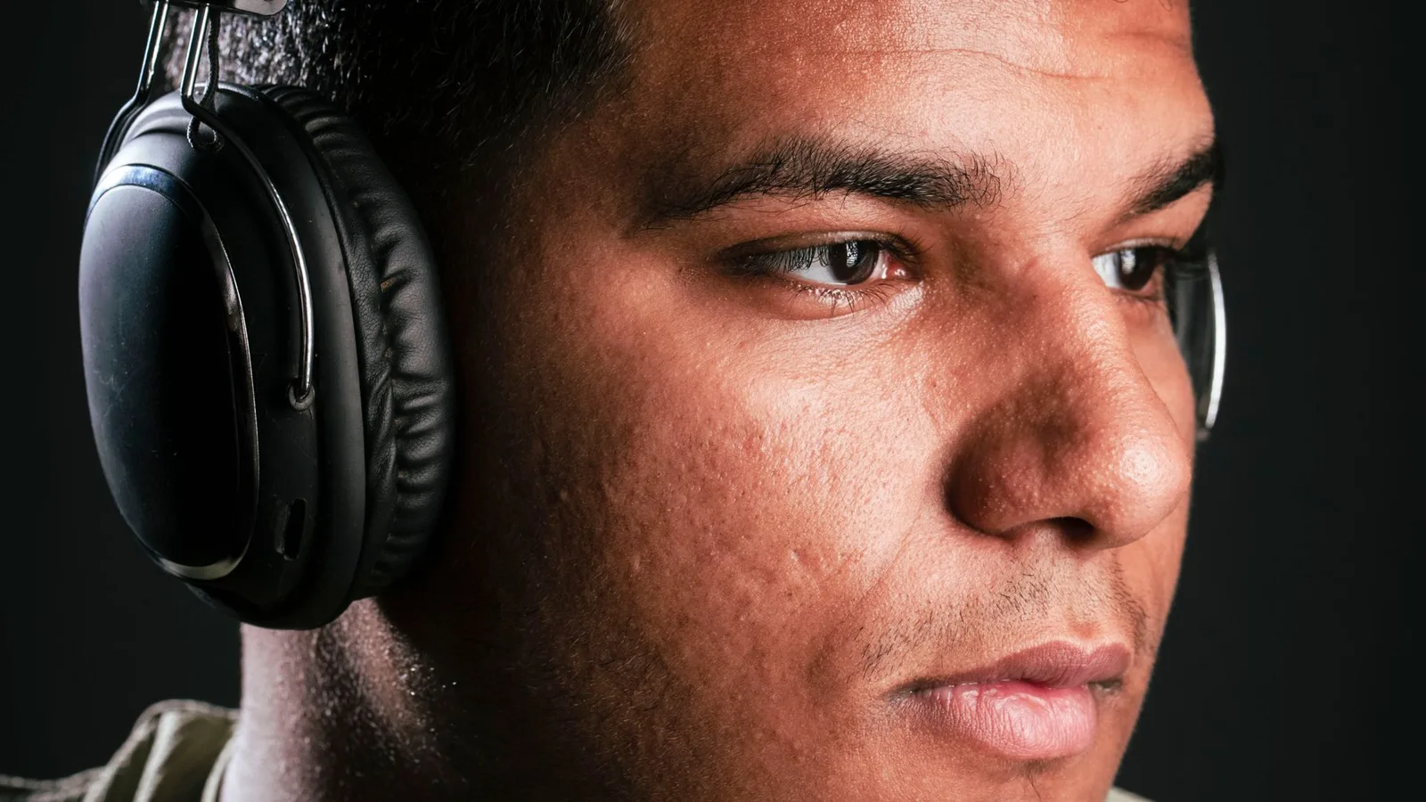 Jovem usando fones de ouvido com expressão de desconforto, ao lado de uma ilustração do ouvido, representando hábitos que prejudicam a audição.