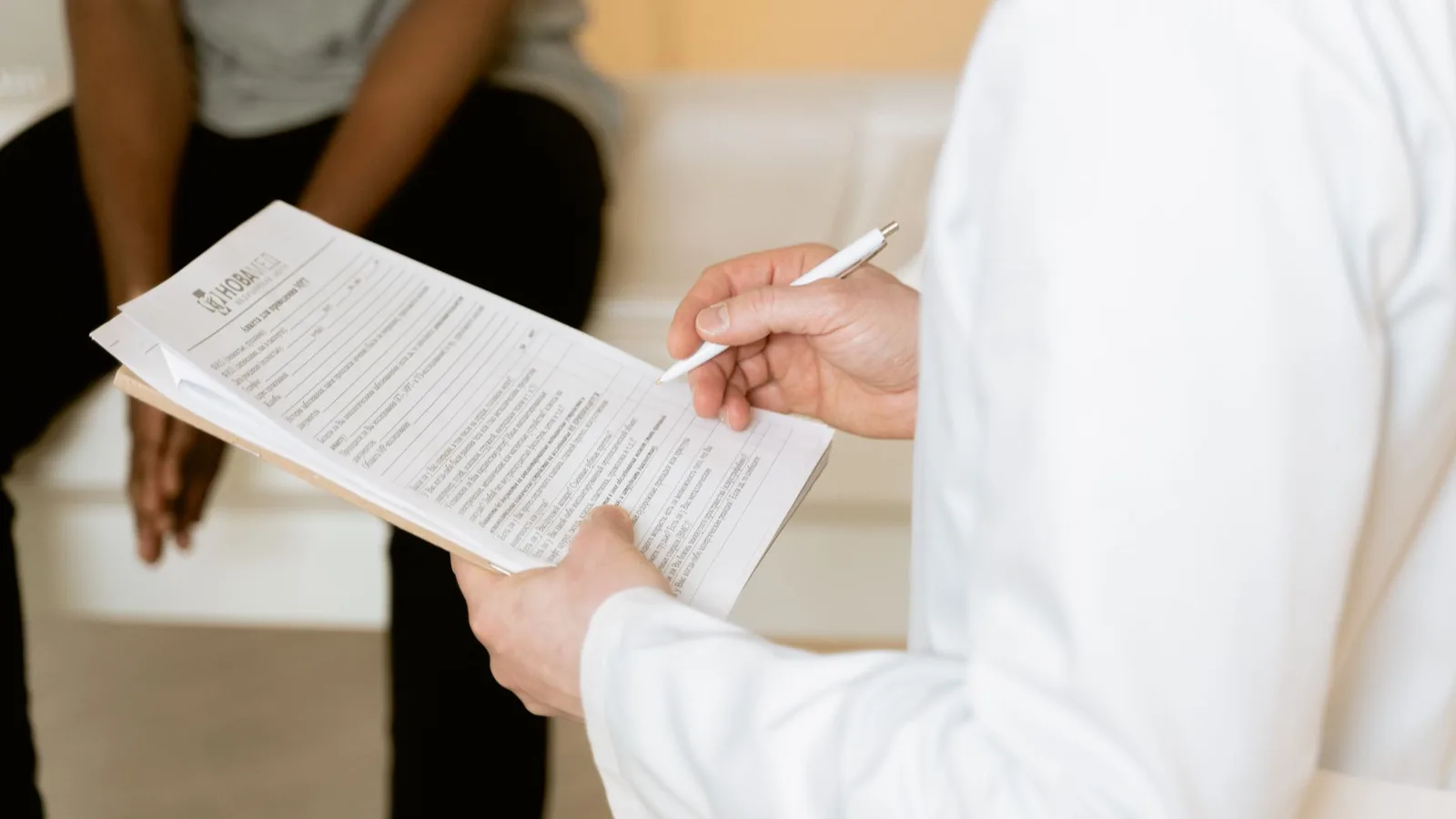 Profissional de saúde de jaleco branco revisando e preenchendo um formulário/laudo médico em prancheta