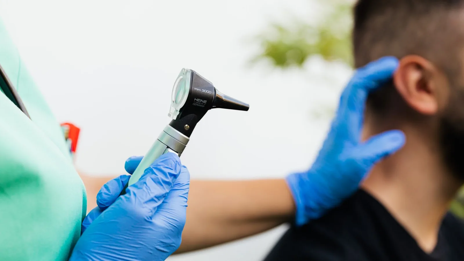 Profissional de saúde com luvas segurando um otoscópio para examinar o ouvido de um paciente adulto
