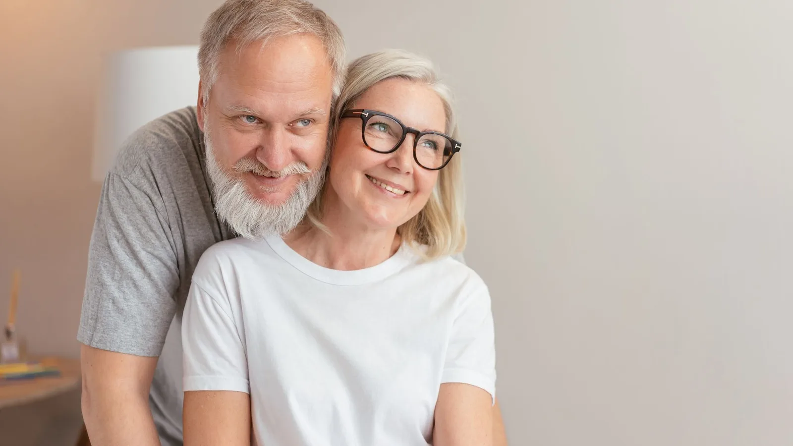Casal de idosos sorrindo, um usando óculos e outro com aparelho auditivo