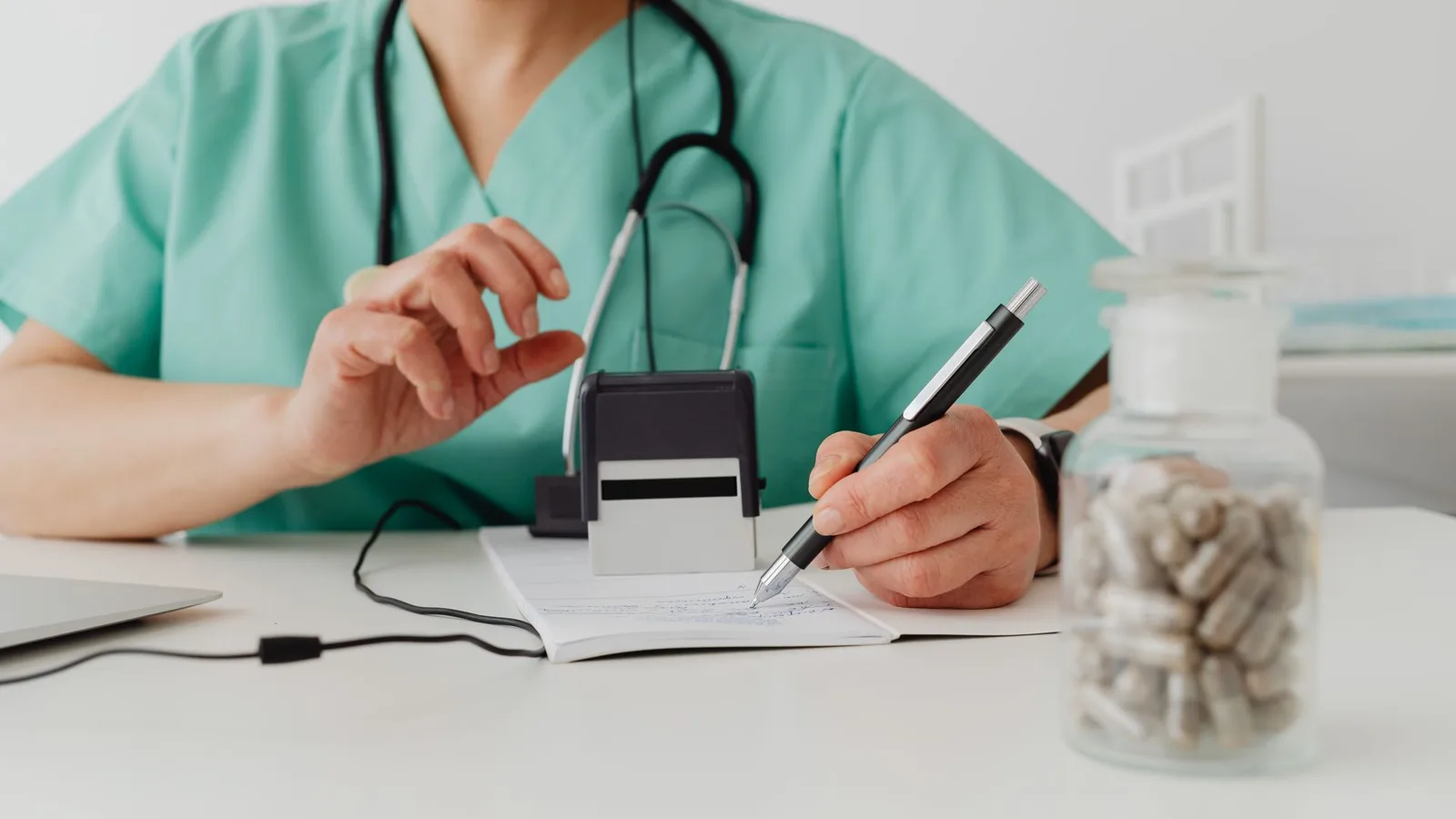 Profissional de saúde escrevendo uma receita médica em consultório, com frasco de medicamentos ao lado
