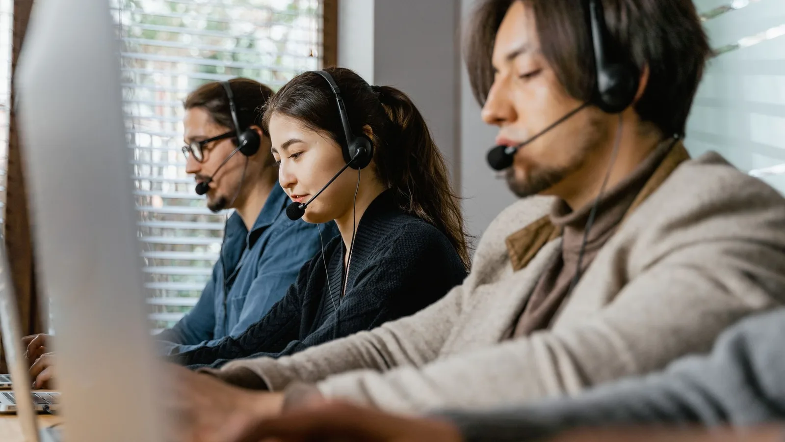 Teleatendente com headset em call center olhando para computador, ilustrando risco de perda auditiva