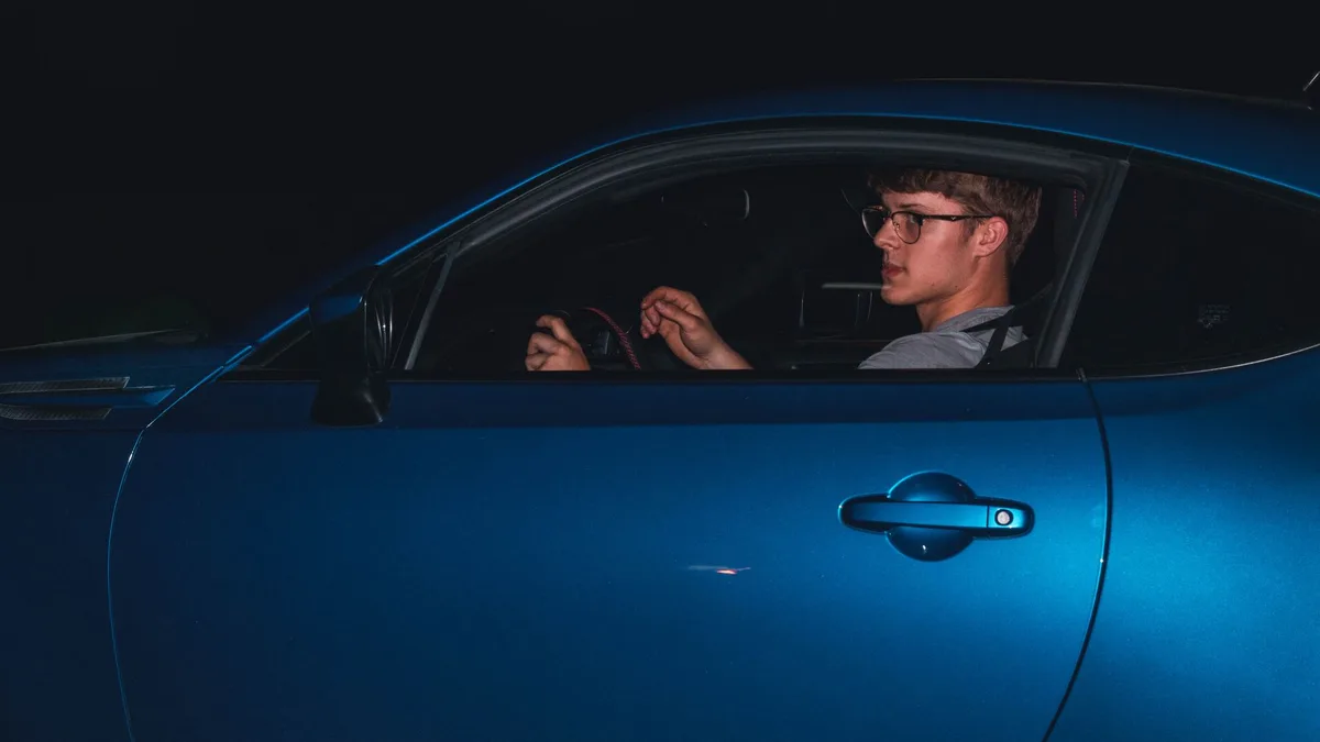 Motorista usando óculos de grau enquanto dirige, com painel do carro ao fundo